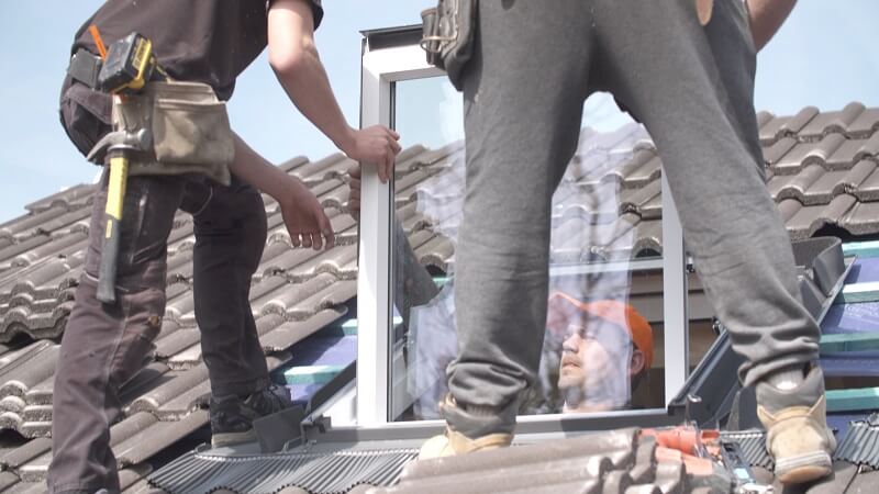 Two professional window installers standing on a roof to install a window