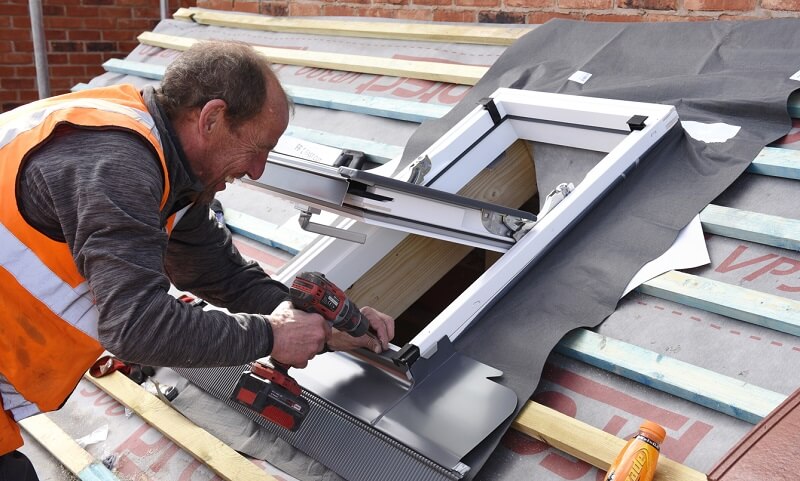 A roofer installing the flashing bottom element around a roof window