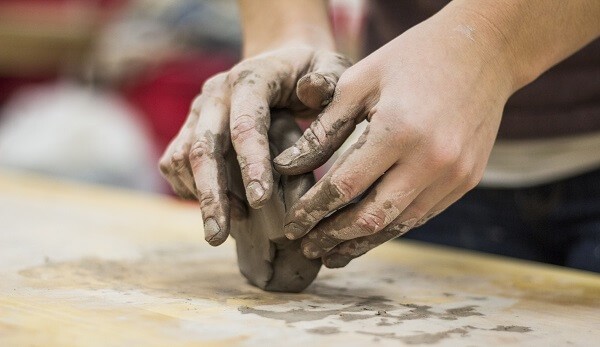 Two hands shaping a lump of clay on a work surface