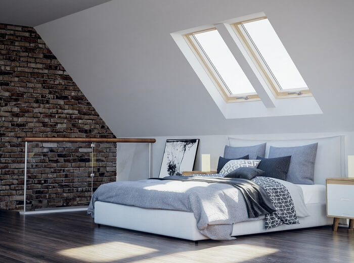 A large bed in an attic conversion with two roof windows above it, lighting it up