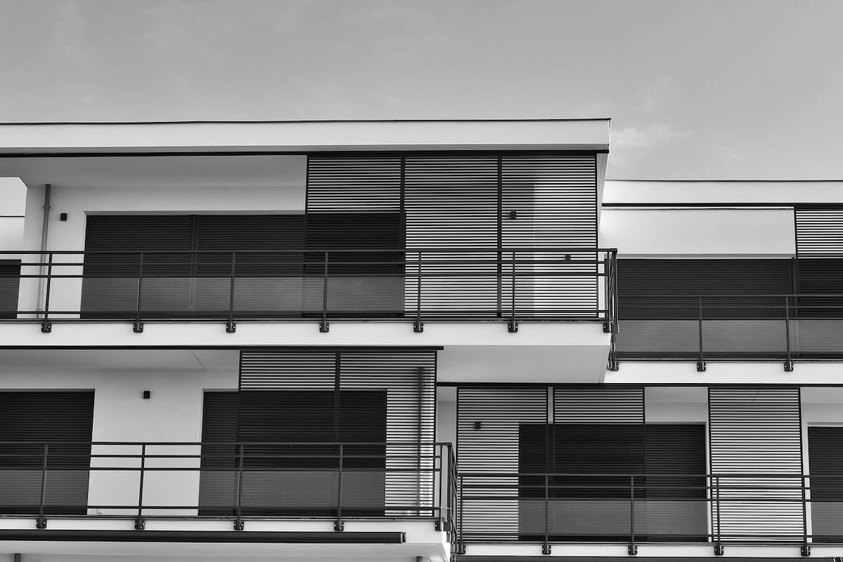 a black and white photo of modern-looking flats. They feature flat roofs, large windows and black slats.