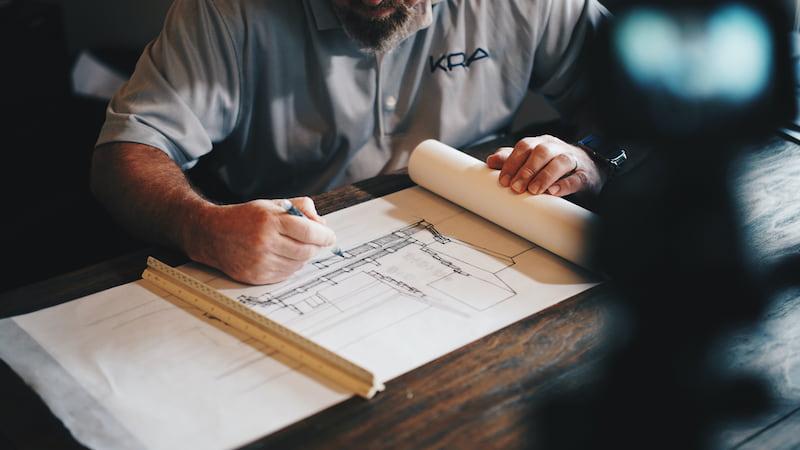 an architect is sat at a desk, drawing some designs on paper