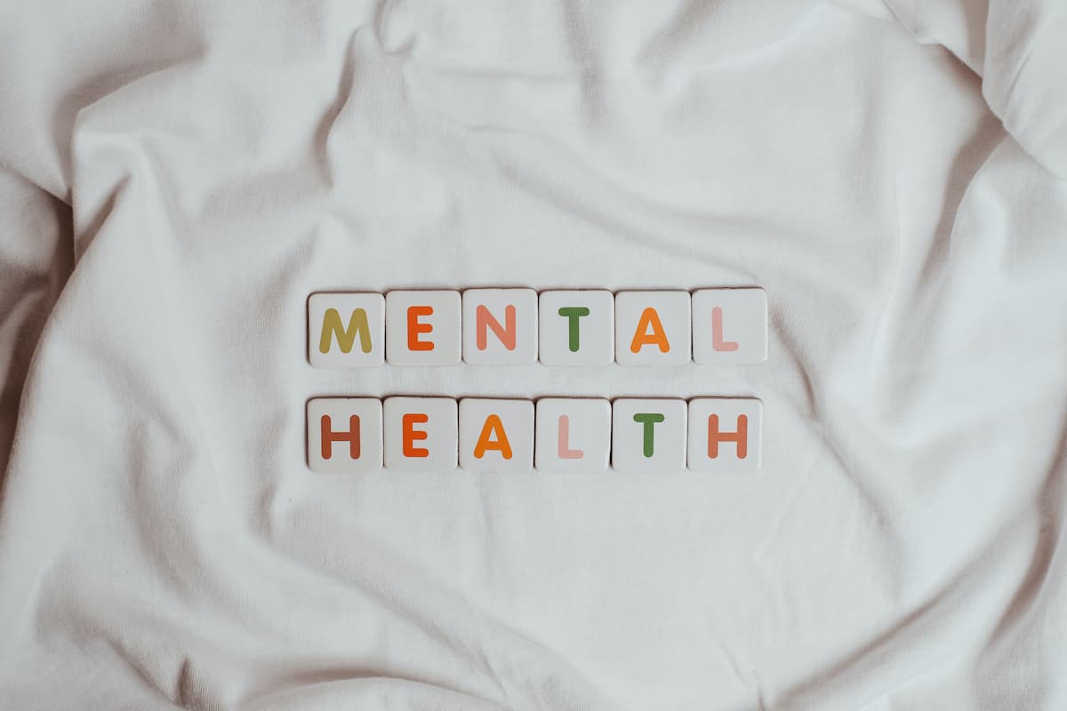 Multicoloured letter tiles on a white cloth background. The tiles spell out the words ‘mental health’